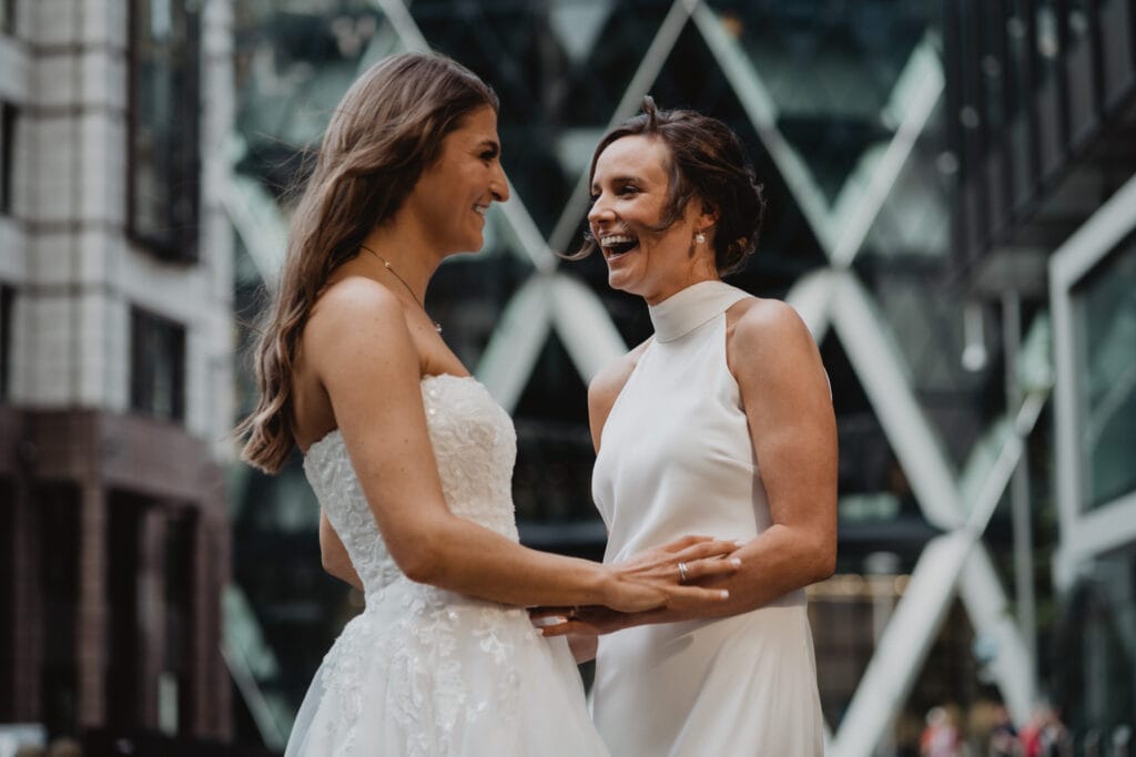 Two brides smiling and laughing in front of The Gherkin