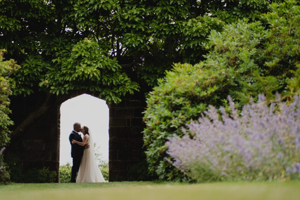 A bride and groom sharing a kiss in the archway of the walled Garden at wadhurst castle